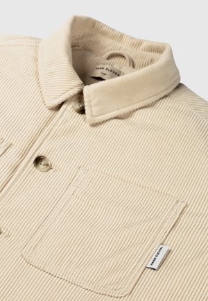 Beige corduroy knoopshirt met een gespreide kraag, borstzak en subtiele verticale ribbelstructuur met merketiket.