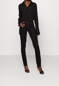 Zwarte doorschijnende overhemd met een gekreukte textuur en lange mouwen, gecombineerd met zwarte slim-fit cargobroeken met zijzakken.