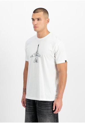 Man wearing a white t-shirt with a detailed aircraft diagram printed on the front, paired with dark gray jeans, standing against a white background.