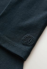 Mörkblå bomull långärmad plagg med ribbad mudd och broderad logotyp på ärmen. Mjuk textur och fina sömnadsdetaljer.