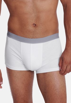 Torso masculin portant un boxer blanc avec une ceinture grise sur un fond clair uni.