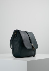 Mörkgrön läderaxelväska med ett lock, detaljer i guld, och en lång justerbar rem. Slät textur, rektangulär form.