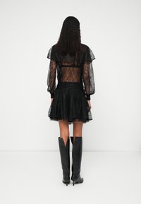 Černé krajkové šaty s průhlednými dlouhými rukávy, volánkovým výstřihem, obepnutým korzetem a rozšířenou sukní. V kombinaci s černými vysokými botami s výřezovými detaily.