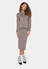 Grijze gebreide top met lange mouwen en knopen, gecombineerd met een bijpassende midi pencil skirt. Zwarte hakken en grijs gestreepte sokken maken de outfit compleet.