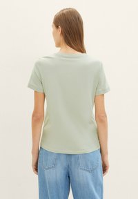 T-shirt vert clair avec un col rond, des manches courtes et une coupe ajustée, associé à un jean bleu clair ample.