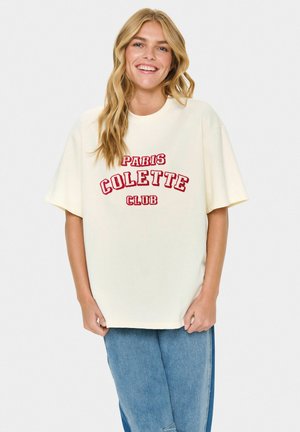 T-shirt oversize de couleur crème en tissu coton, avec du texte brodé rouge : "PARIS COLETTE CLUB." Manches courtes et coupe décontractée.