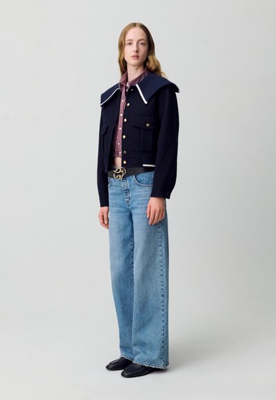 Chaqueta recortada navy con gran cuello, botones dorados, combinada con una camisa de cuadros, jeans anchos azules y zapatos negros. Acentos de diseño simples.