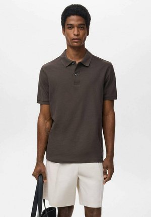 Dunkelbraunes Polohemd mit klassischem Kragen, einer Knopfleiste mit zwei Knöpfen und kurzen Ärmeln. Kombiniert mit weißen Shorts und einer schwarzen Tasche.