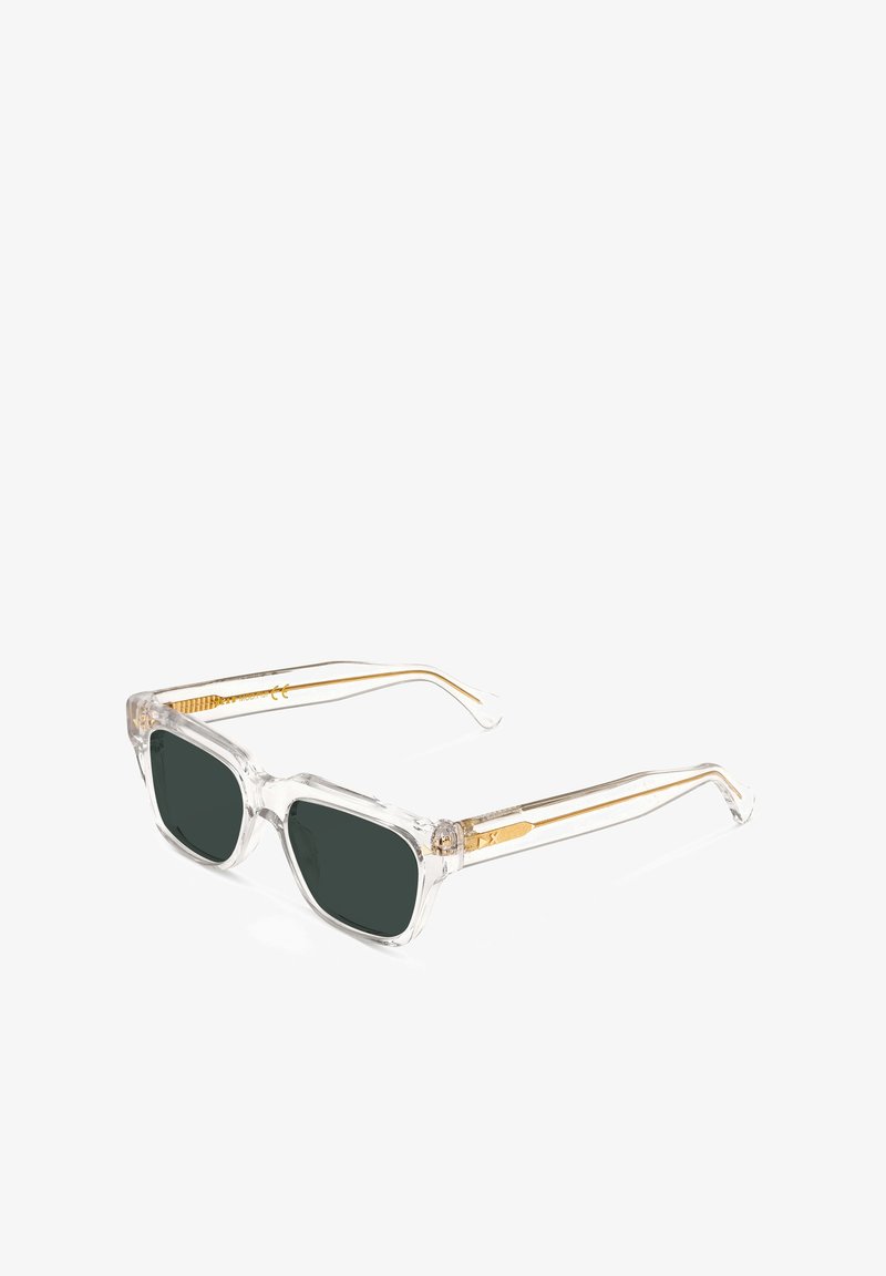 Occhiali da sole con montatura trasparente e lenti verde scuro; tempietti con accenti dorati e un design testurizzato. Struttura robusta con forma angolare.
