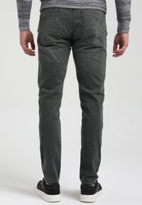 Vaqueros ajustados de color gris oscuro con bolsillos traseros; tejido texturizado; combinados con zapatillas negras con suela blanca. Fondo liso.