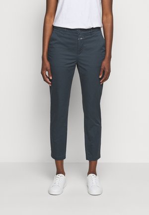 Pantalones ajustados cortos de color azul oscuro combinados con zapatillas blancas y una camisa blanca por dentro, mostrados desde la mitad del torso hasta los pies.