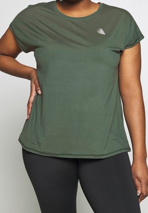Femme portant un t-shirt à manches courtes vert olive avec un petit logo géométrique blanc près de l'encolure et un legging noir, debout avec la main sur la hanche.