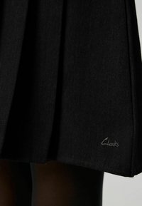Gonna nera plissettata realizzata in tessuto testurizzato, con cuciture sottili. Logo "Clarks" ricamato vicino all'orlo.