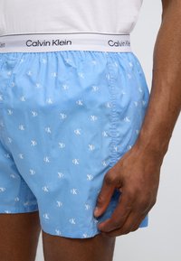 Ανοιχτό μπλε ανδρικά εσώρουχα από βαμβάκι, με επαναλαμβανόμενο λευκό μοτίβο λογοτύπου "ck". Η μέση είναι μαύρη με τη λευκή επιγραφή "Calvin Klein".