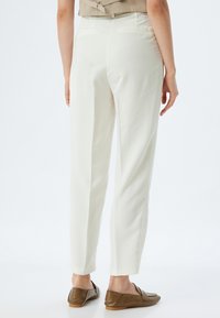 Pantaloni bianchi su misura con taglio slim e gamba leggermente affusolata. Design pulito, tessuto soffice e tasche posteriori discrete. Indossati con mocassini marroni.