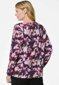 Langärmliges Oberteil aus transparentem Stoff mit einem lila und pinken Blumenmuster. Rundhalsausschnitt und Raffung auf der Rückseite.