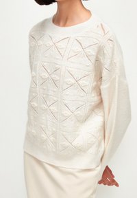 Maglione lavorato a maglia color crema con motivi a diamante testurizzati, dotato di scollatura rotonda e maniche dalla vestibilità rilassata, realizzato in tessuto morbido e leggero.