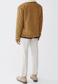 Bruine corduroy jas met een crèmekleurige kraag, gedragen over een marineblauwe shirt, gecombineerd met lichtgekleurde broeken en beige enkellaarzen.