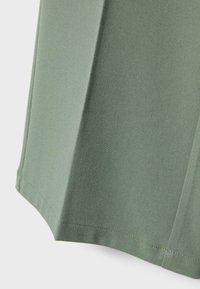 Tissu vert à la texture lisse avec un léger éclat. Présente un bord plié et des coutures visibles, créant des lignes nettes et une forme structurée.