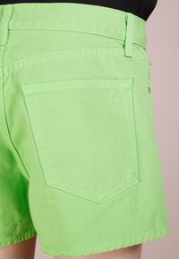 Shorts en denim vert vif avec une poche arrière sculptée et des coutures contrastées. Les bords sont festonnés pour une finition texturée.