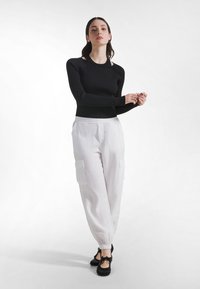 Schwarzes, geripptes Langarmoberteil kombiniert mit leichten weißen Cargohosen mit seitlichen Taschen und elastischen Bündchen, getragen mit schwarzen Schuhen.