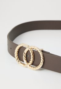 Cinturón de cuero marrón con dos hebillas circulares entrelazadas en tono dorado. Textura suave con agujeros ajustables para un mejor ajuste.