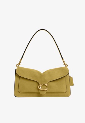 Sac à épaule en daim jaune moutarde avec fermoir "C" doré et bandoulière bordée de noir, avec une étiquette logo Coach sur le côté.