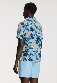 Kortärmad skjorta i ljusblått med ett blommönster i mörkblått och persika. Bärs med ljusblå shorts, som har en avslappnad passform.