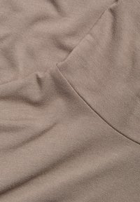 Beige bomullstyg med en fin ribbstruktur, som visar släta veck och en böjd sömdetalj längs kanten.