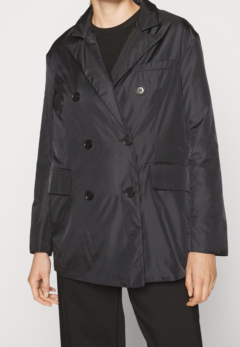 Veste double boutonnage bleu marine foncé avec une texture lisse et brillante, deux poches avant, grands boutons noirs et revers crantés.