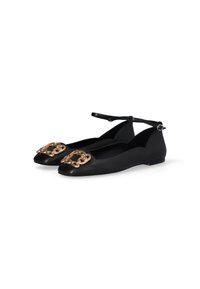 Scarpe flat nere con dettaglio in catena dorata sulla punta e sottili cinturini alla caviglia con piccole fibbie, mostrate affiancate su sfondo bianco.