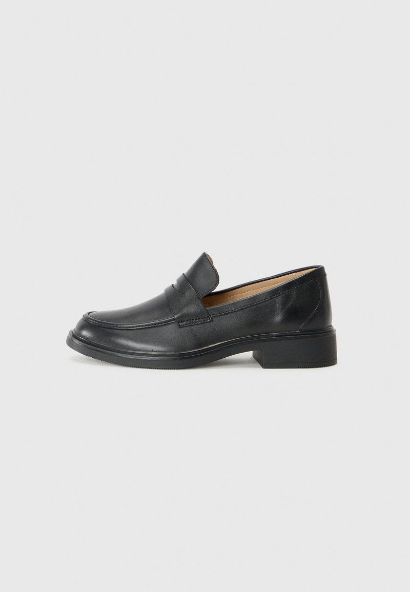 Mocassino in pelle nera con tacco basso, caratterizzato da un design cucito e stile slip-on, posizionato su uno sfondo bianco uniforme.