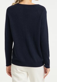Marineblaue Sweatshirt mit langen Ärmeln, gerippter Textur, rundem Ausschnitt und seitlichen Schlitzen; minimalistische Designakzente auf der Rückseite.