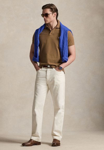 Καφέ μπλουζάκι πόλο, μπεζ τζιν, μπλε πλεκτό πουλόβερ περασμένο στους ώμους, καφέ δερμάτινα παπούτσια και γυαλιά ηλίου, με ασημένιο ρολόι στον καρπό.