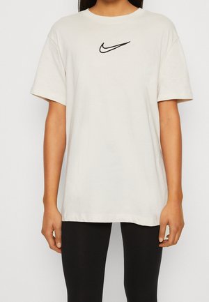 Camiseta de algodón color crema con el logo negro de Nike en el pecho. Tiene mangas cortas y un corte holgado.
