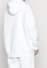 Vit huvtröja med lös passform, mjuk textur och ribbade muddar. Designen har en enfärgad baksida och minimal detaljering.