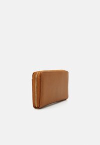 Portefeuille en cuir marron avec une texture lisse et une fermeture éclair dorée. Sa forme rectangulaire présente un bord cousu et un design compact.