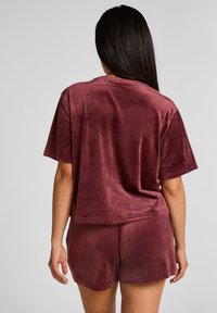 Bordeaux velours lounge set met een T-shirt met korte mouwen en shorts. Zachte textuur met een ontspannen pasvorm en een gebogen zoomdetail.