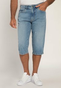 Pantalones cortos de mezclilla en azul claro, de longitud a la rodilla con dobladillo deshilachado, cinco bolsillos y ligero desgaste. Combinados con zapatillas blancas.