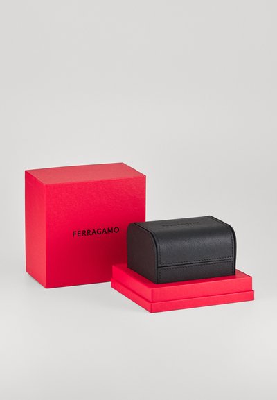 Must must kullast ehituskast, mille ümar ülaosa, tekstureeritud pind ja kontrastsed punased kastid all, millel on "FERRAGAMO" bränding.