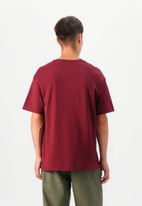 T-shirt bordeaux à manches courtes, en coton, avec un col rond et une coupe décontractée, associé à un pantalon vert olive.