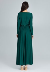 Maxi-jurk met lange mouwen van diep groene stof, met een ontspannen pasvorm, een getailleerde taille en een gladde textuur, gecombineerd met huidkleurige hakken.