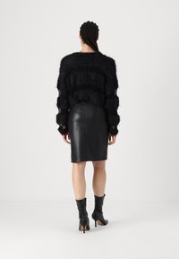 Μαύρο φuzzy cropped πουλόβερ με υφή πλέξης, σε συνδυασμό με μαύρη δερμάτινη μίνι φούστα. Το μοντέλο φοράει μαύρες γόβες με τακούνι.