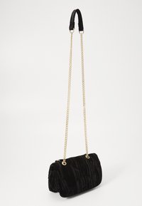 Borsa a tracolla in velluto nero con design trapuntato, tracolla in catena dorata e texture morbida, dotata di chiusura a zip sicura e piccolo dettaglio del logo.