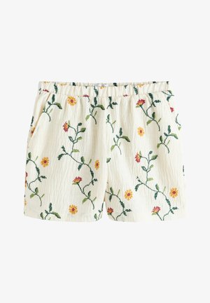 Shorts couleur crème avec une ceinture élastique, décorés de vignes vertes brodées et de petites fleurs jaunes et rouges.