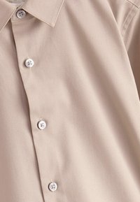 Beige skjorta med krage i slätt tyg, försedd med sex vita knappar framtill, med en subtil lyster och minimalistisk design.