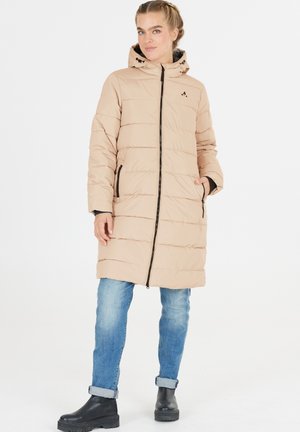 Manteau rembourré beige avec un design matelassé horizontal, fermeture éclair et capuche. Présente des accents noirs et des poches latérales. Porté sur un jean bleu.