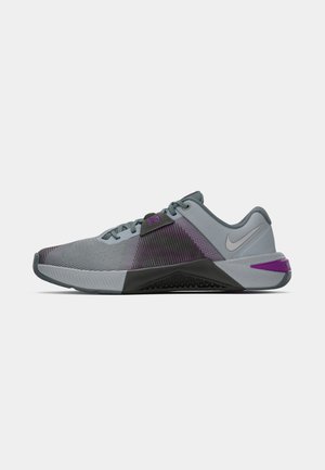 Pantofi sport Nike cu un superior din plasă gri, accente purpurii și o talpă din cauciuc texturat negru, proiectați pentru performanță și confort.