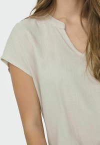 Jasno beżowa lniana bluzka z krótkimi rękawami, delikatnym dekoltem w kształcie litery V oraz teksturowanym wykończeniem, prezentująca luźny i przewiewny fason.