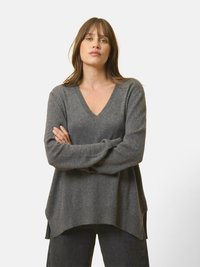 Szary, oversize sweter z głębokim dekoltem w serek, wykonany z miękkiego materiału. Posiada długie rękawy, ściągacz u dołu oraz luźny krój z bocznymi rozcięciami.